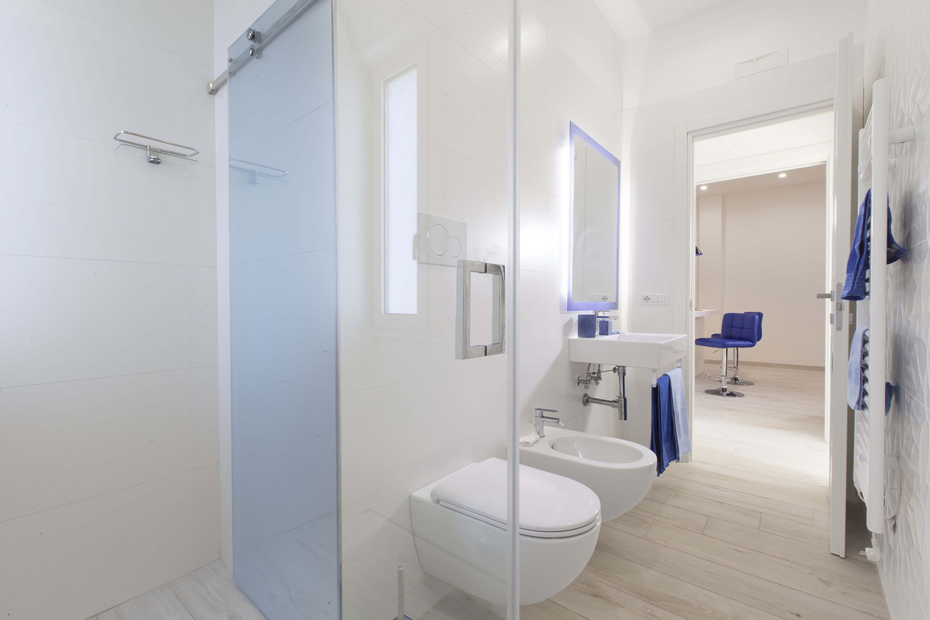 Een moderne badkamer met een glazen douchecabine, toilet, bidet en een wastafel met spiegel erboven.