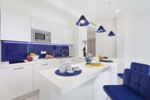 Une cuisine moderne avec des meubles blancs, un four à micro-ondes encastré et des luminaires suspendus bleus.
