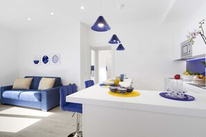 Um espaço de estar moderno com um sofá azul, uma ilha de cozinha branca e iluminação pendente.