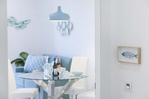 Un espace de salle à manger moderne avec une table en verre, des chaises blanches, un canapé bleu et une suspension.