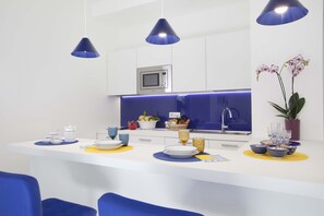 Cozinha moderna com ilha central, luminárias pendentes azuis e micro-ondas acima.