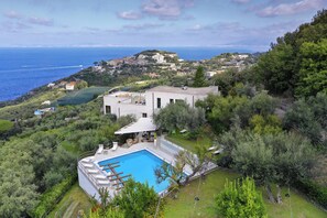 Eine Villa mit Swimmingpool, umgeben von üppiger Vegetation und mit Blick auf eine Küstenstadt.