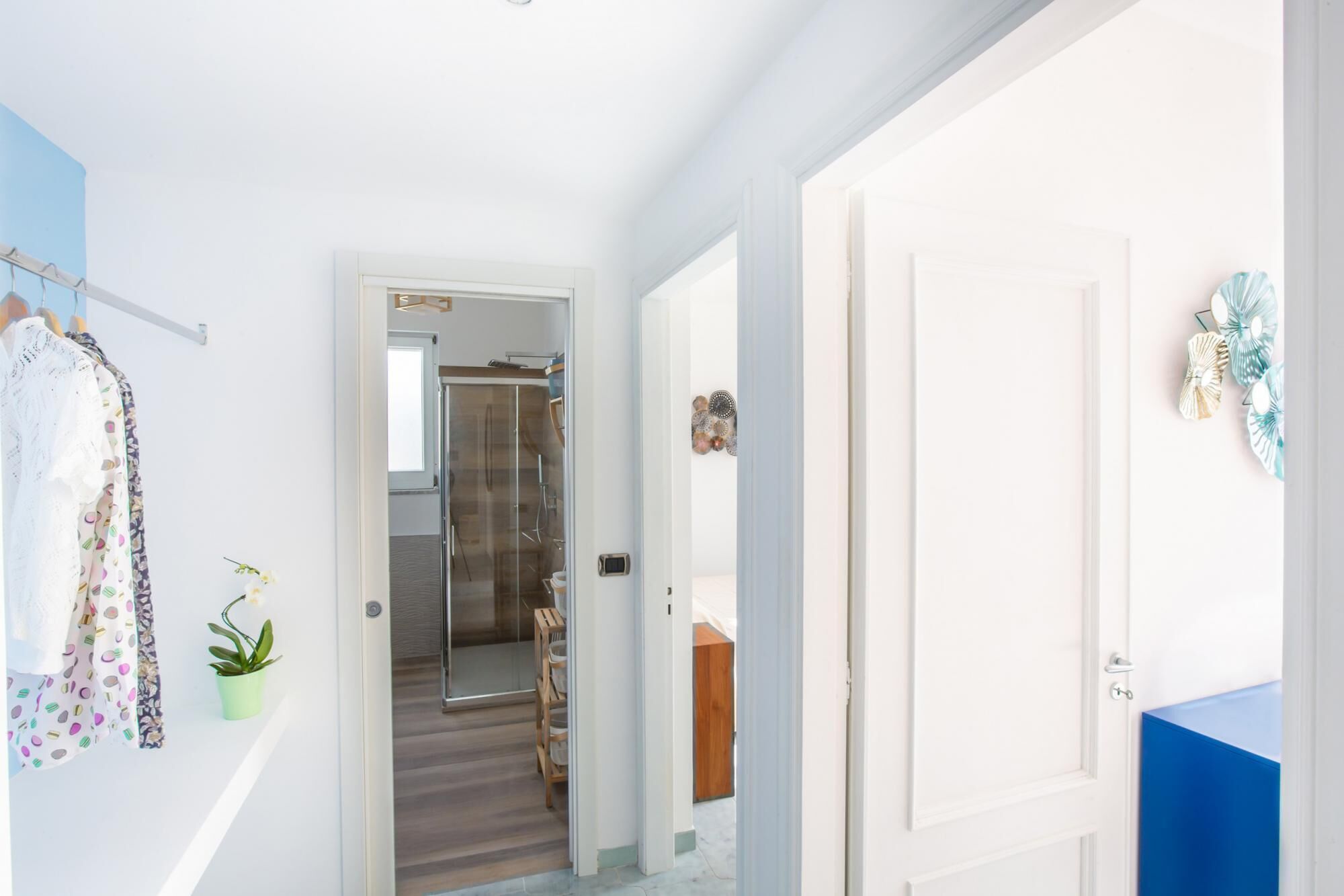 A hallway with a glass shower door, a wooden door, and a blue wall.