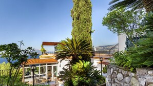 Ein Gebäude an der Küste mit einer Steinmauer, einer Palme und Blick aufs Meer.