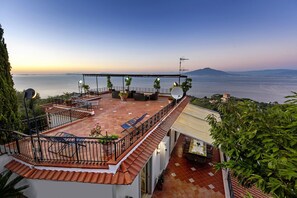 Eine Dachterrasse mit Außenmöbeln, Blick auf das Meer und ein Berg in der Ferne.