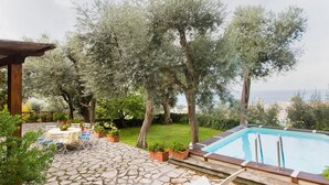 A stone patio with outdoor furniture, a swimming pool, and olive trees. - Villa Stella in Massa Lubrense (Massa Lubrense)