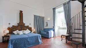 A bedroom with a wooden headboard bed, a blue sofa, a chair, and a staircase. - Villa Stella in Massa Lubrense (Massa Lubrense)
