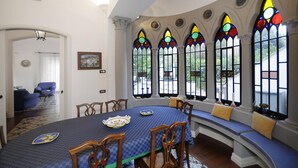A dining area with a round table, wooden chairs, and a bench with cushions. There are stained glass windows with colorful designs. - Villa Angelo in Sant Agnello (Sant'Agnello)