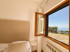 A bedroom with a bed, a window with a view of a beach and the sea, and a radiator. - Villa Raffaella in Sant Agata sui Due Golfi (Massa Lubrense)