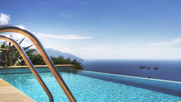 An infinity pool with clear blue water, a metal pool ladder, and a view of the ocean and distant mountains. - Villa Raffaella in Sant Agata sui Due Golfi (Massa Lubrense)