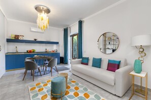 A modern living room with a white sofa, a round mirror, and a dining area with a table and chairs. - Appartamento Sorrento Suite de Charme 2 (Sorrento)