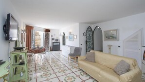 A living room with a sofa, a television, a dining area with chairs and a table, and a staircase leading to another room. - Villa Isabel in Praiano (Praiano)