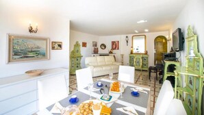 A dining area with a table set for four, a sofa, and a TV in the background. - Villa Isabel in Praiano (Praiano)