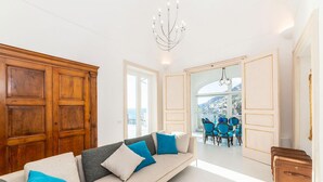 A modern living room with a sofa, a chandelier, and a view of a dining area with blue chairs.
