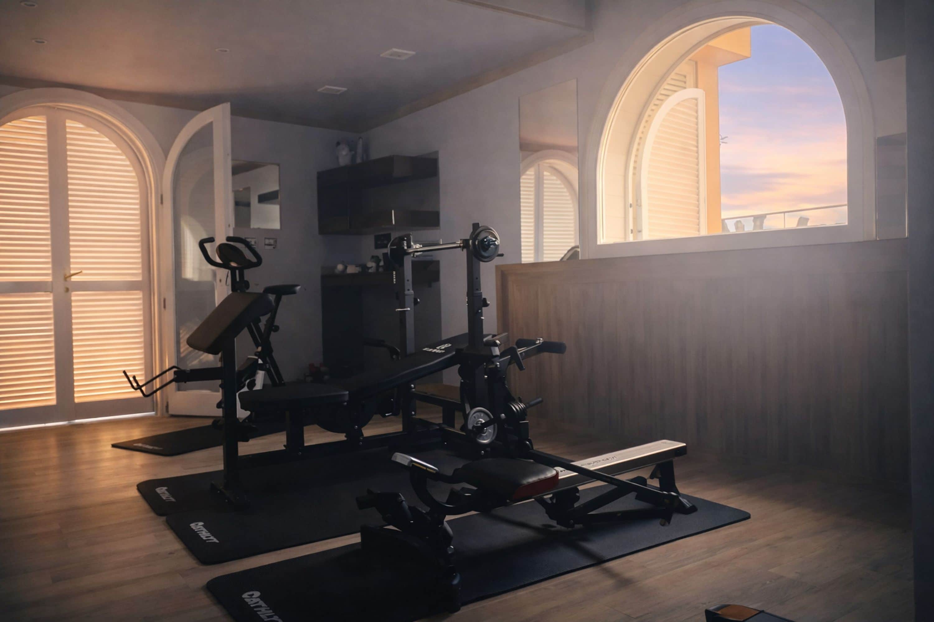 A gym with exercise equipment, wooden flooring, and large arched windows.