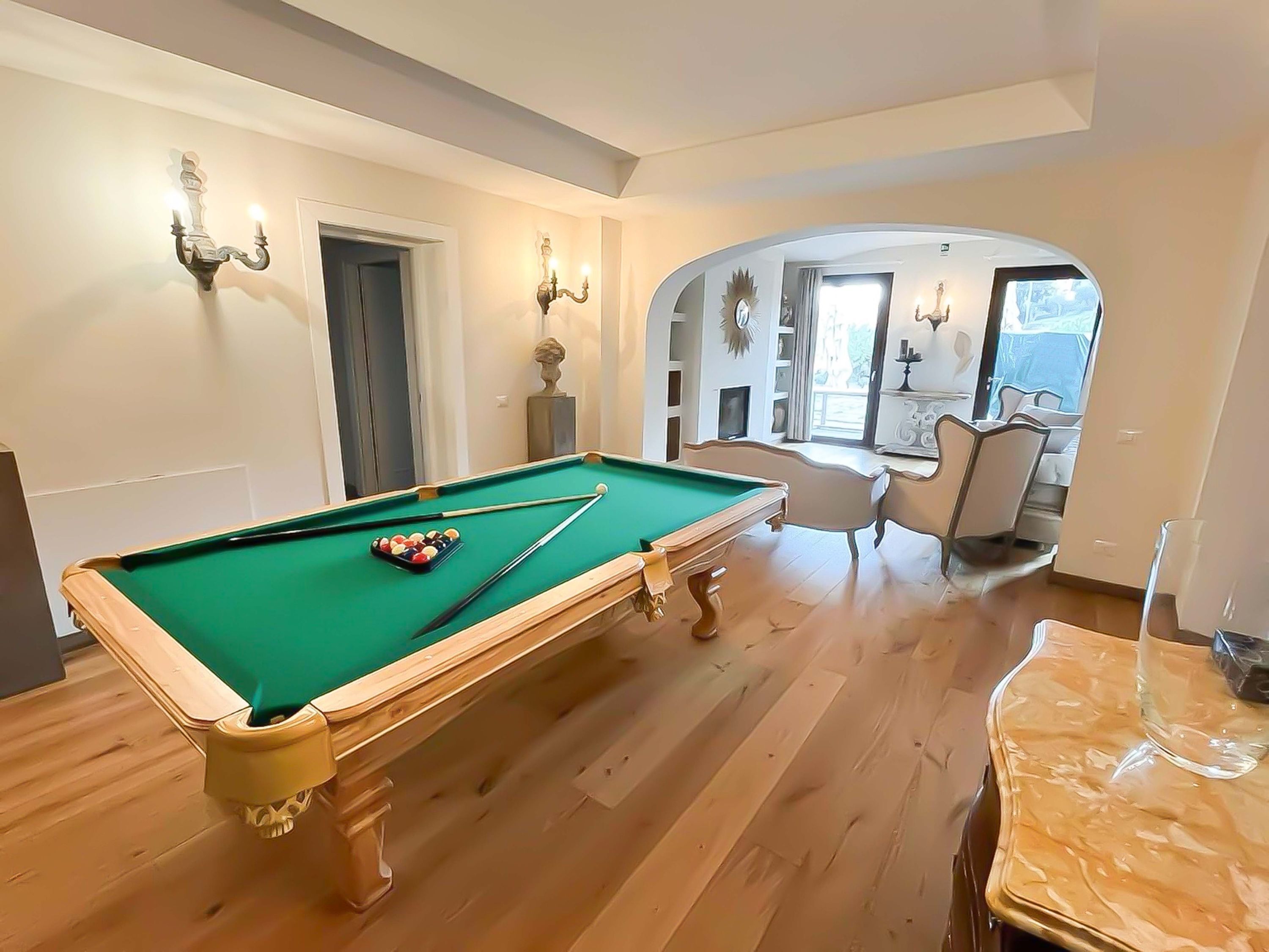 A pool table in a room with wooden flooring, a door, and a window.