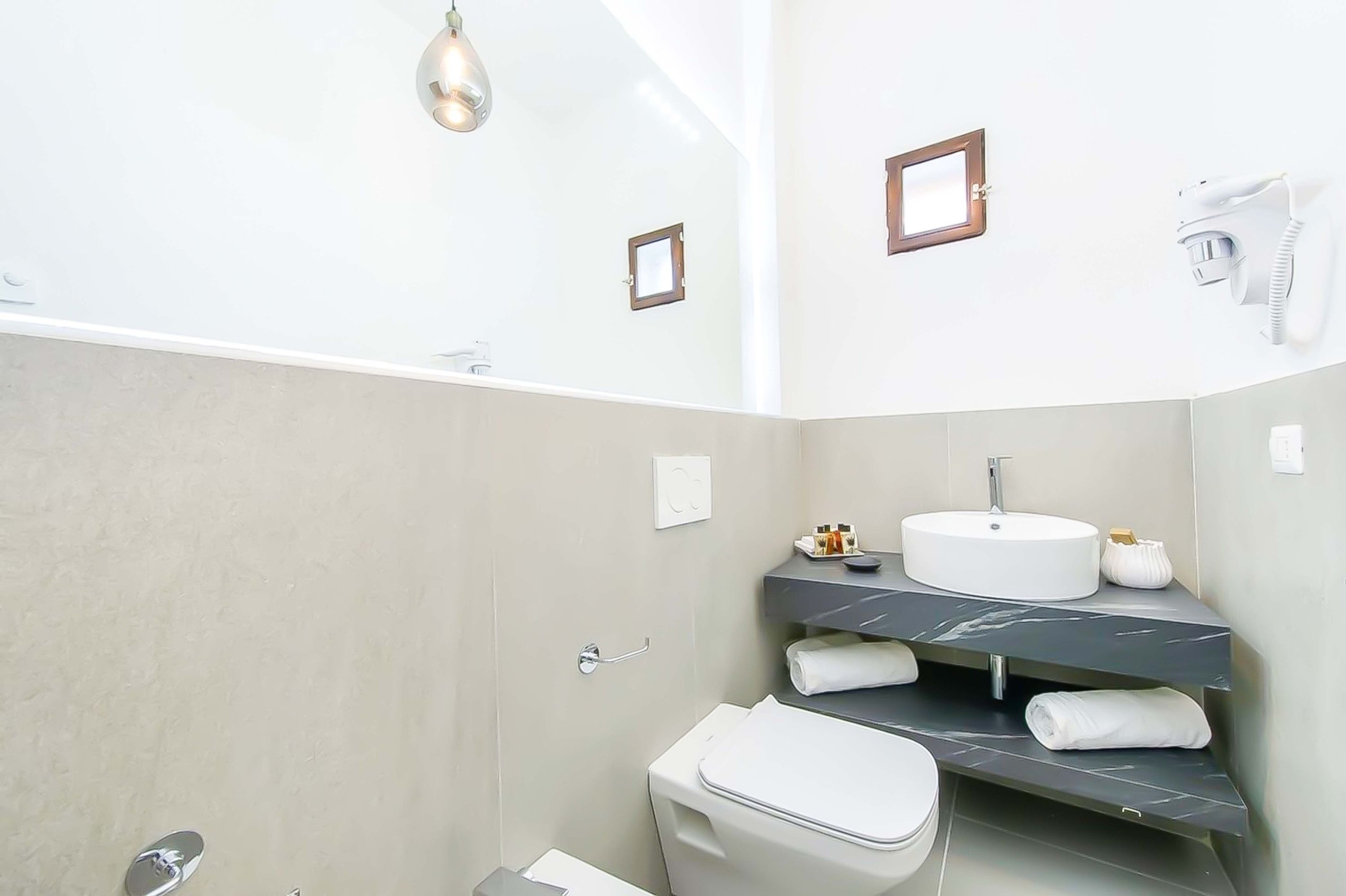 Ein modernes Badezimmer mit Waschbecken, Waschtisch und Toilette. Auf dem Waschtisch liegen Handtücher und Pflegeprodukte, und ein Fön ist an der Wand montiert.