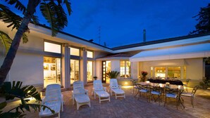 Un patio moderno al aire libre con sillones de descanso y una zona de comedor, rodeado por un edificio blanco con ventanas amplias.