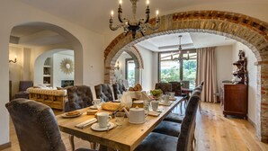 A dining area with a long wooden table, upholstered chairs, and a chandelier. - Ville Il Paradiso in Panzano (Greve in Chianti)