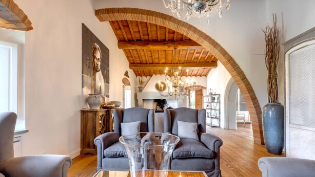 A spacious living room with a high wooden ceiling, a chandelier, and a large vase on a wooden coffee table. - Ville Il Paradiso in Panzano (Greve in Chianti)
