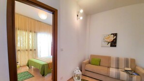 A living room with a sofa, a green rug, a small table, and a bed with a green tablecloth. - Casa Alice 1 Bedrooms Apartment in Alghero (Alghero)