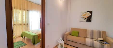 Un salon avec un canapé, un tapis vert, une petite table et un lit recouvert d’une nappe verte.