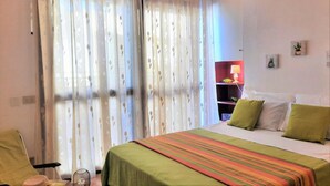 A hotel room with a bed, a chair, a lamp, and a window with curtains. - Casa Alice 1 Bedrooms Apartment in Alghero (Alghero)