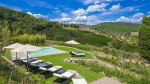 Uma área de piscina com espreguiçadeiras e guarda-sóis, cercada por vegetação exuberante e uma paisagem ondulada.