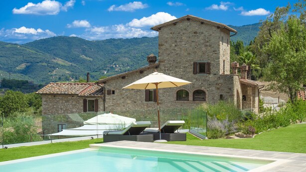 Uma villa de pedra com piscina, espreguiçadeiras e guarda-sol.