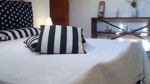 Una cama bien hecha con almohadas a rayas, una puerta de madera y un pequeño estante con adornos.