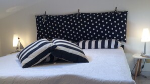 Una cama bien tendida con almohadones a rayas y un cabecero de lunares. Hay dos lámparas de noche y una mesita con una lámpara encima.