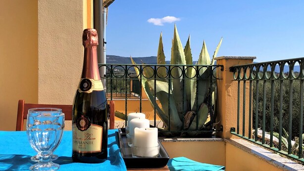 A table with a bottle of wine, glasses, candles, and a blue tablecloth on a balcony with a view of cacti and mountains. - Casa Ilaria 2 Bedrooms Apartment in Alghero (Alghero)