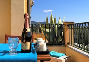 Ett bord med en vinflaska, glas, ljus och en blå duk på en balkong med utsikt över kaktusar och berg.