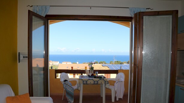 Un balcon avec une table et des chaises, une vue sur la mer et un bâtiment équipé de panneaux solaires.