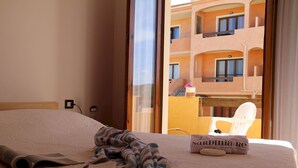 Une chambre d’hôtel avec un lit, une fenêtre donnant sur un immeuble et une chaise à l’extérieur.