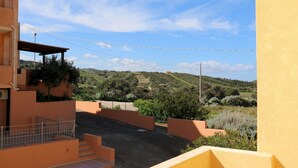 Un immeuble résidentiel doté d’un balcon, d’une allée pavée et offrant une vue sur un paysage vallonné.