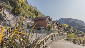 A hillside residential area with houses, a paved road, and a rocky cliff. - La Dolce Vista in Perledo (Perledo)