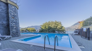 A rectangular pool with two ladders, surrounded by a stone wall and a paved deck. - La Dolce Vista in Perledo (Perledo)