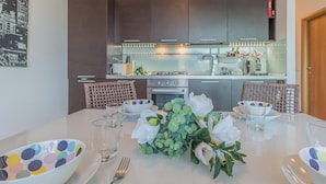 A modern kitchen with dark cabinets, stainless steel appliances, and a dining area with a white table set for four. - La Dolce Vista in Perledo (Perledo)