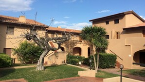 Un patio con una escultura de árbol, una palmera y un edificio con techo de tejas.
