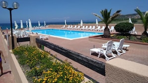 Zona de piscina con sillones de descanso y sombrillas, con vista a un cuerpo de agua.