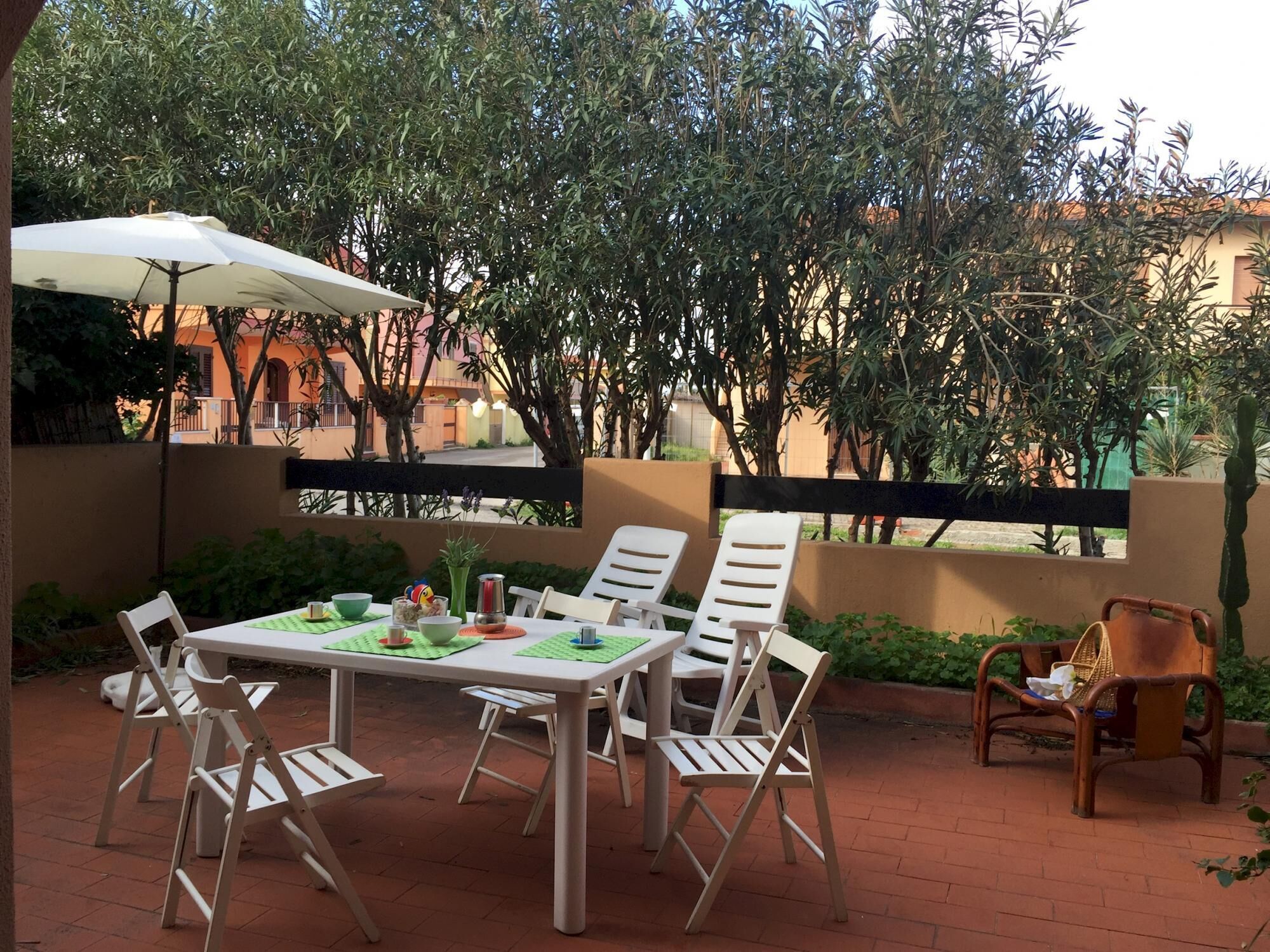 An outdoor patio with a table and chairs, surrounded by greenery and a view of buildings in the background.