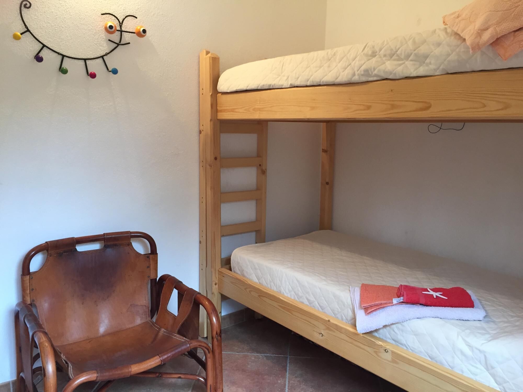 A bunk bed with a wooden frame, a chair with a curved backrest, and a wall decoration.