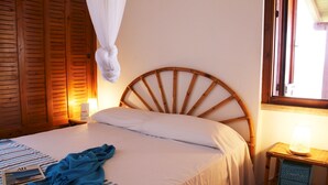 Ein Bett mit hölzernem Kopfteil, einer Nachttischlampe und einem Fenster mit Vorhängen.
