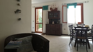 A dining area with a wooden table and chairs, a wicker sofa, and a cabinet with decorative items. - Casa Marta 4 Bedrooms Apartment in Stintino (Stintino)