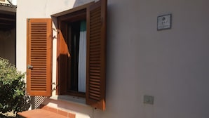 A building with a window with wooden shutters, a brick base, and a sign indicating the address. - Casa Marta 4 Bedrooms Apartment in Stintino (Stintino)