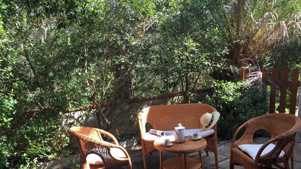 Wicker furniture with cushions and a teapot on a table in a garden setting. - Casa Marta 4 Bedrooms Apartment in Stintino (Stintino)