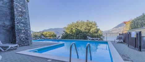Piscina rectangular con dos escaleras, rodeada por un muro de piedra y una terraza empavedada.