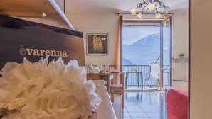 A room with a piano, a white floral arrangement, a table with plates and glasses, and a view of mountains through a balcony door. - Patrizia s House Varenna (Varenna)