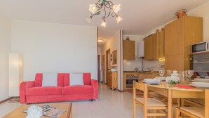 A modern living room with a red sofa, wooden dining table, and a kitchen area with wooden cabinets and a microwave. - Patrizia s House Varenna (Varenna)